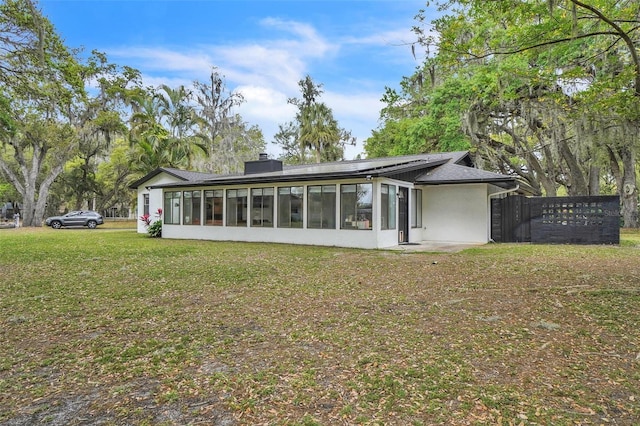 back of house featuring a sunroom, a chimney, and stucco siding