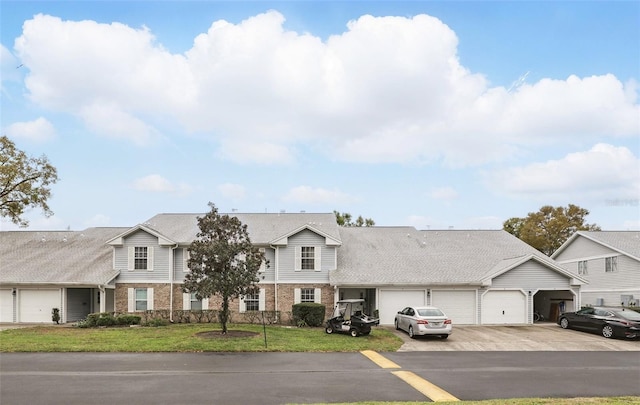 view of property featuring a front lawn, roof with shingles, concrete driveway, a garage, and brick siding