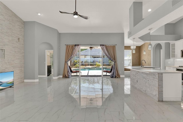 living area featuring baseboards, arched walkways, a ceiling fan, marble finish floor, and a high ceiling