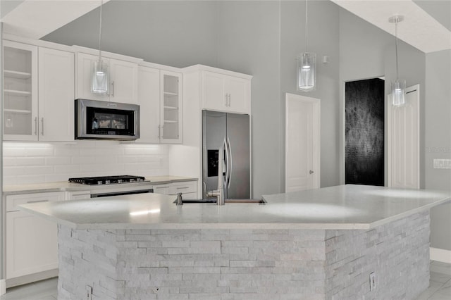 kitchen with stainless steel appliances, white cabinets, a large island, decorative backsplash, and decorative light fixtures