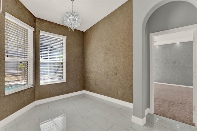 spare room featuring arched walkways, baseboards, marble finish floor, wallpapered walls, and an inviting chandelier