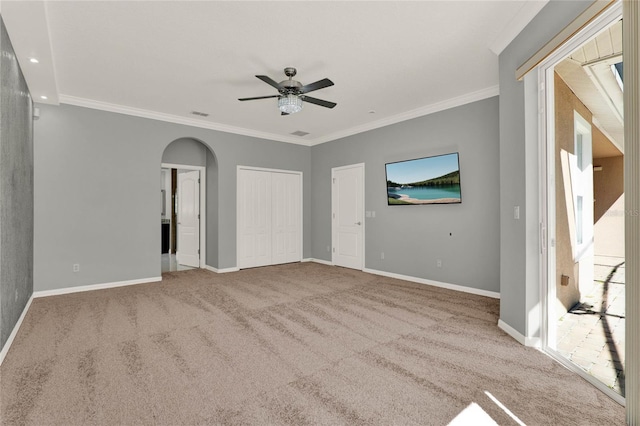 carpeted spare room with arched walkways, crown molding, visible vents, a ceiling fan, and baseboards