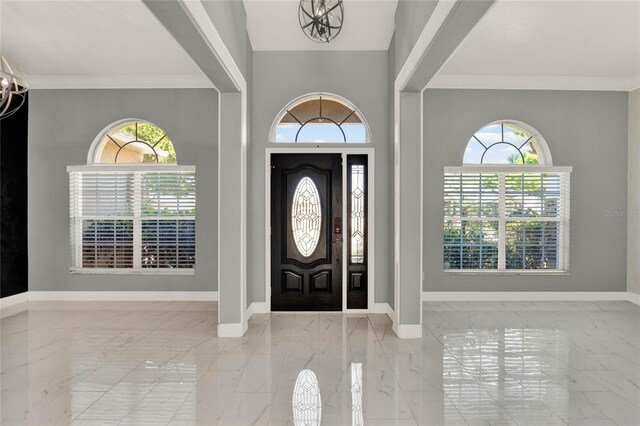 foyer entrance with ornamental molding, marble finish floor, and baseboards