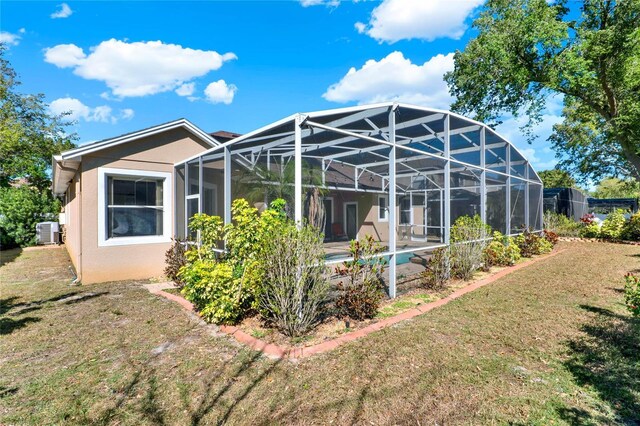 back of property with a lawn, glass enclosure, a swimming pool, central AC, and stucco siding