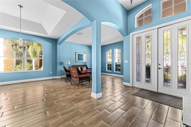 entryway with an inviting chandelier, wood tiled floor, arched walkways, and baseboards