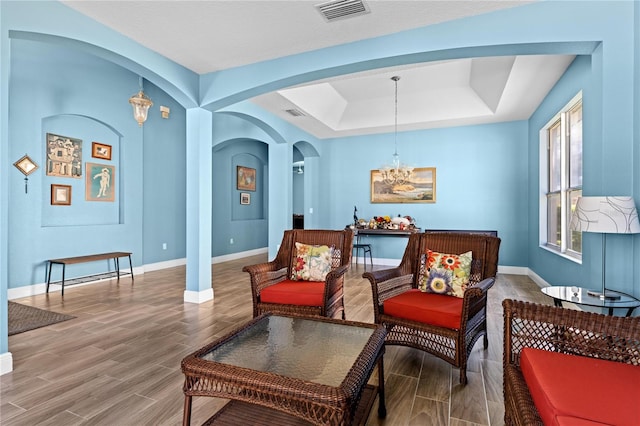 sitting room with wood tiled floor, baseboards, visible vents, and a tray ceiling