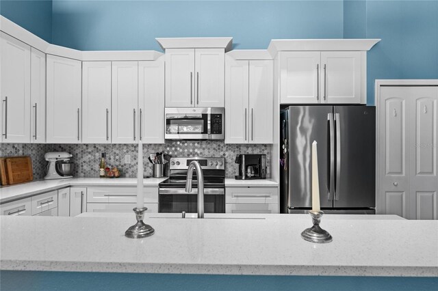 kitchen with light stone counters, decorative backsplash, appliances with stainless steel finishes, white cabinetry, and a sink