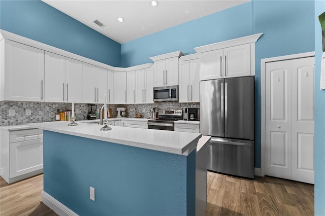 kitchen featuring decorative backsplash, an island with sink, appliances with stainless steel finishes, light wood-style floors, and white cabinetry