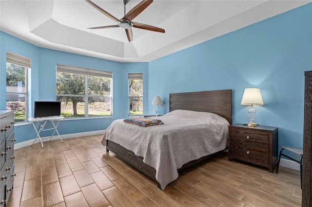 bedroom with baseboards, a raised ceiling, a ceiling fan, wood tiled floor, and a textured ceiling