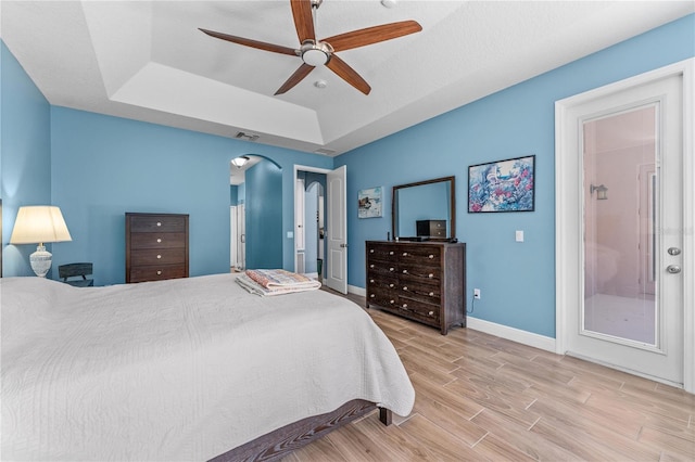 bedroom with arched walkways, a tray ceiling, visible vents, wood finished floors, and baseboards