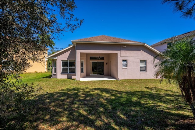 rear view of property featuring stucco siding, a lawn, a ceiling fan, and a patio