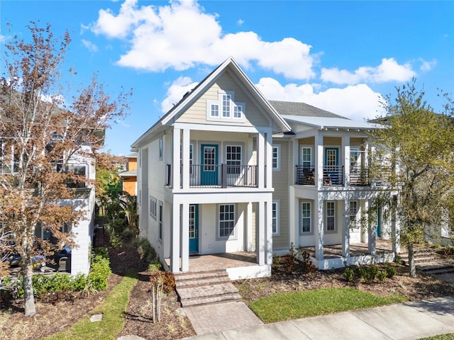 greek revival house with stucco siding, a balcony, and a porch