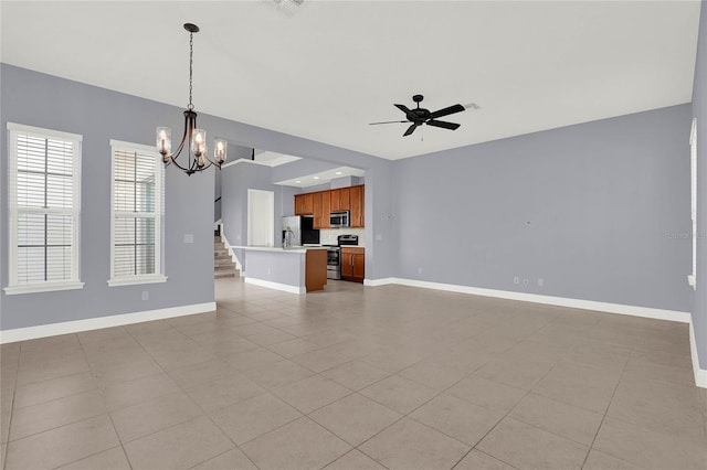 unfurnished living room featuring stairs, light tile patterned floors, ceiling fan with notable chandelier, and baseboards