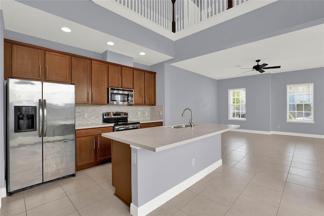 kitchen featuring light tile patterned floors, a ceiling fan, a sink, appliances with stainless steel finishes, and brown cabinets