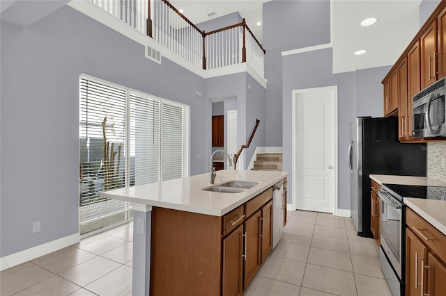 kitchen with a sink, appliances with stainless steel finishes, a kitchen island with sink, and light tile patterned flooring