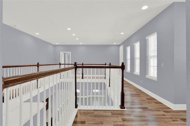 corridor with recessed lighting, baseboards, wood finished floors, and an upstairs landing