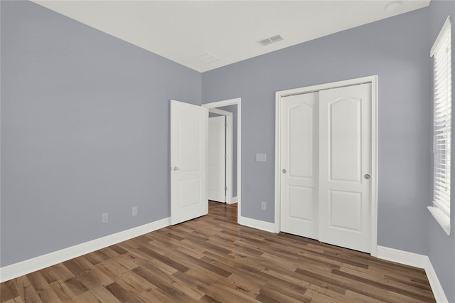 unfurnished bedroom featuring a closet, visible vents, baseboards, and wood finished floors