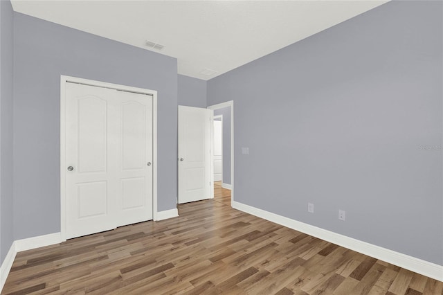 unfurnished bedroom with visible vents, baseboards, a closet, and wood finished floors