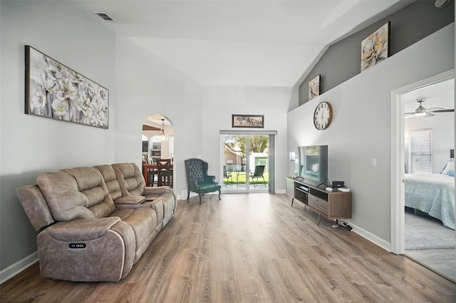 living area featuring arched walkways, high vaulted ceiling, wood finished floors, visible vents, and baseboards