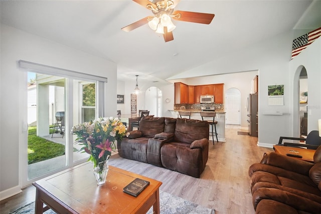 living area with light wood finished floors, baseboards, arched walkways, a ceiling fan, and vaulted ceiling