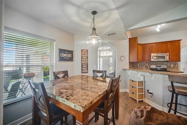 dining space featuring arched walkways, dark wood finished floors, lofted ceiling, visible vents, and a textured ceiling