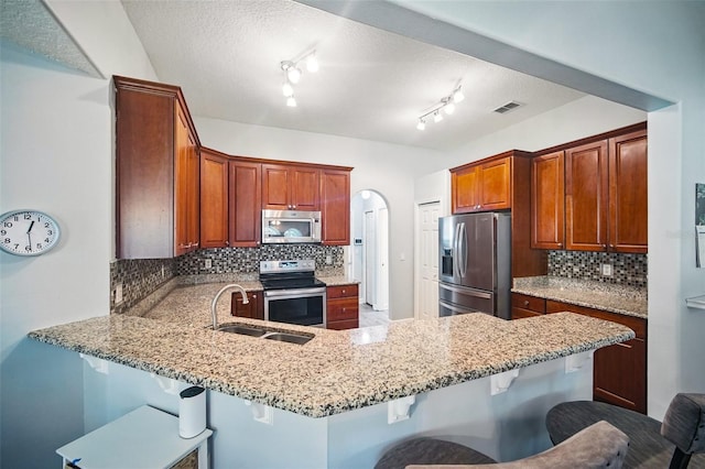 kitchen featuring visible vents, appliances with stainless steel finishes, a peninsula, light stone countertops, and a sink