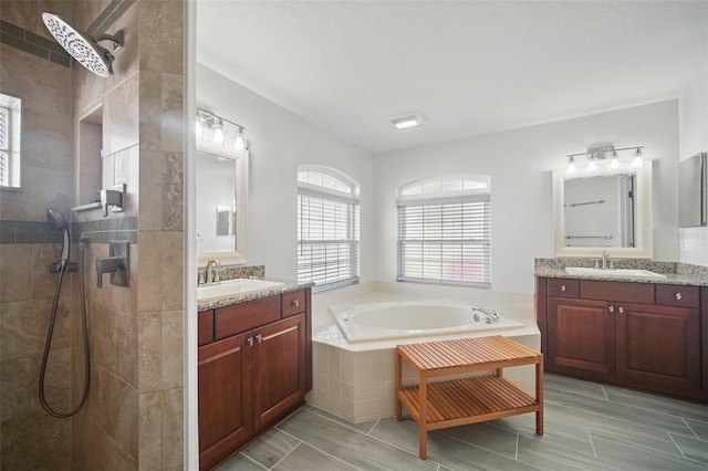 bathroom with a walk in shower, two vanities, a sink, and a bath