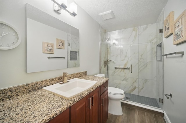 bathroom featuring a marble finish shower, toilet, wood finished floors, a textured ceiling, and vanity