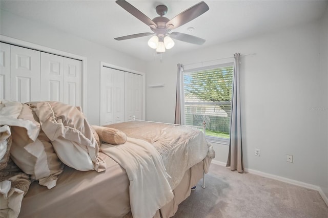 bedroom featuring a ceiling fan, baseboards, multiple closets, and light colored carpet