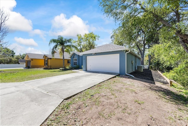 ranch-style home with driveway, an attached garage, central air condition unit, a front lawn, and stucco siding