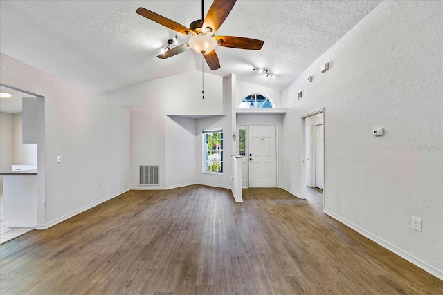 entrance foyer with a textured ceiling, wood finished floors, visible vents, baseboards, and vaulted ceiling