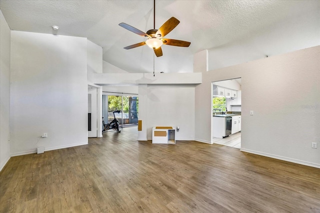 unfurnished living room with a textured ceiling, ceiling fan, high vaulted ceiling, a sink, and light wood finished floors