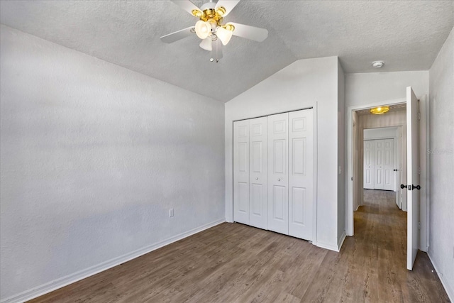 unfurnished bedroom with a closet, vaulted ceiling, a textured ceiling, wood finished floors, and baseboards