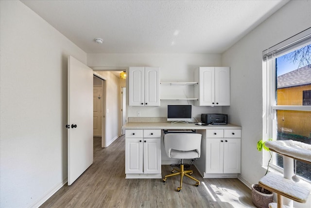 home office with built in desk, light wood-style floors, baseboards, and a textured ceiling