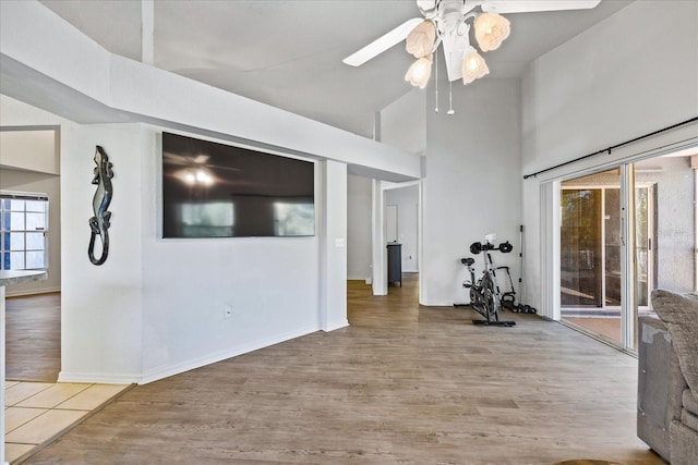 exercise room featuring ceiling fan, wood finished floors, a towering ceiling, and baseboards