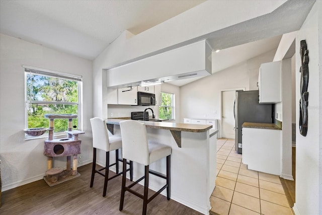 kitchen featuring black microwave, lofted ceiling, a peninsula, a sink, and white cabinetry