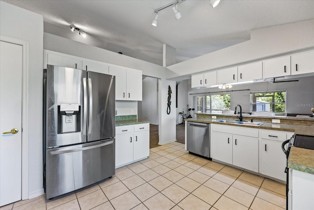 kitchen featuring appliances with stainless steel finishes, light tile patterned flooring, a sink, and white cabinetry