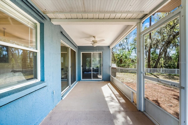 unfurnished sunroom featuring a ceiling fan, plenty of natural light, and beamed ceiling