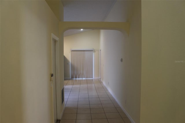 hall with light tile patterned floors, arched walkways, lofted ceiling, and baseboards