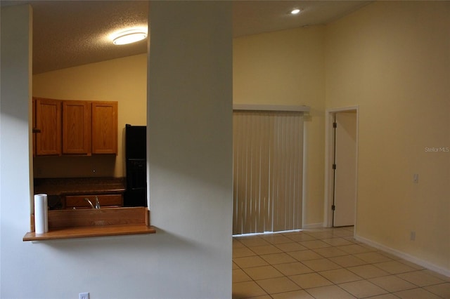 interior space with lofted ceiling, light tile patterned floors, a textured ceiling, and baseboards