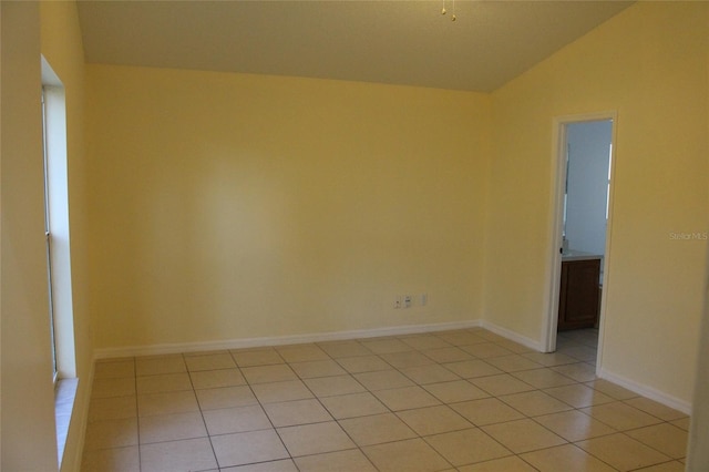 empty room featuring vaulted ceiling, light tile patterned flooring, and baseboards