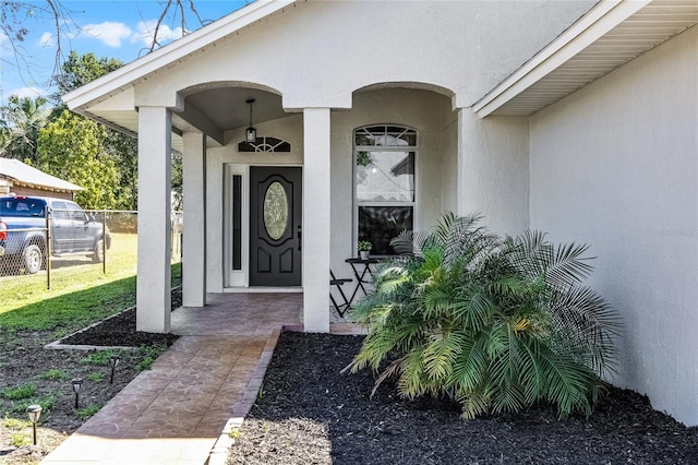 doorway to property featuring stucco siding, a yard, a porch, and fence