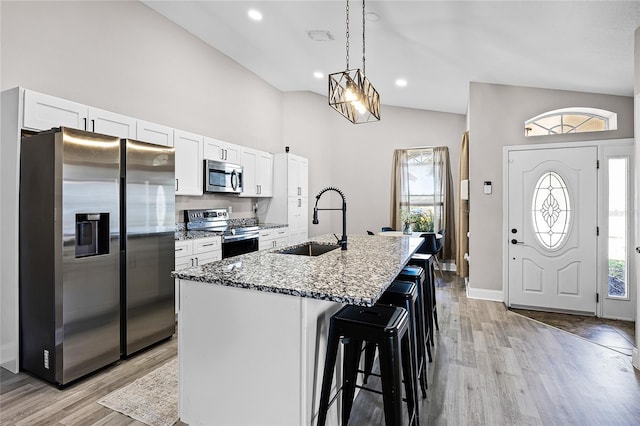 kitchen with light stone counters, a center island with sink, a sink, appliances with stainless steel finishes, and white cabinetry