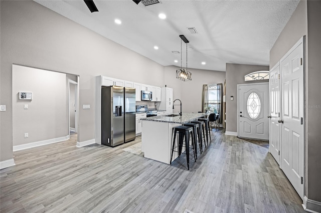 kitchen featuring a kitchen bar, visible vents, a sink, white cabinetry, and stainless steel appliances