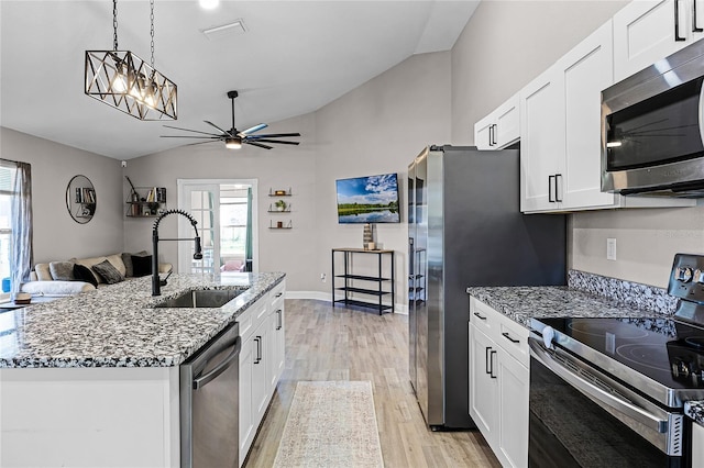 kitchen with light wood-style flooring, a sink, light stone counters, appliances with stainless steel finishes, and lofted ceiling