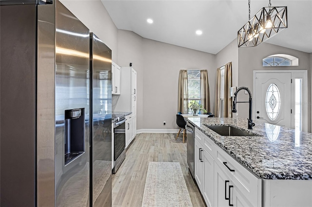 kitchen with light wood finished floors, lofted ceiling, stone counters, appliances with stainless steel finishes, and a sink