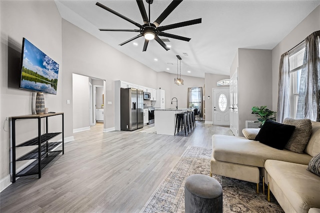 living room with baseboards, light wood-type flooring, recessed lighting, high vaulted ceiling, and a ceiling fan