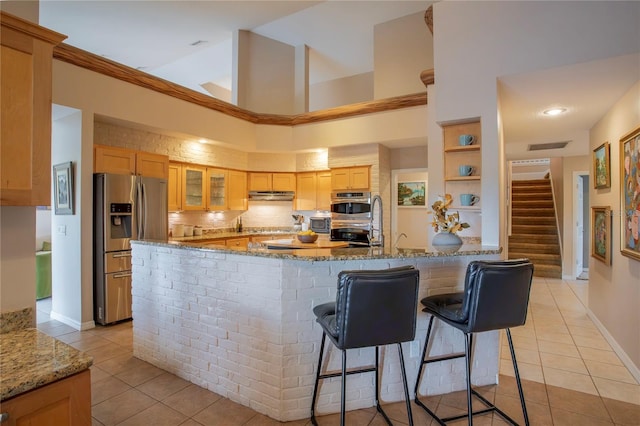 kitchen with light tile patterned floors, glass insert cabinets, appliances with stainless steel finishes, and under cabinet range hood