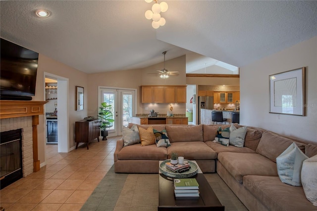 living area with a ceiling fan, a textured ceiling, light tile patterned flooring, lofted ceiling, and a brick fireplace