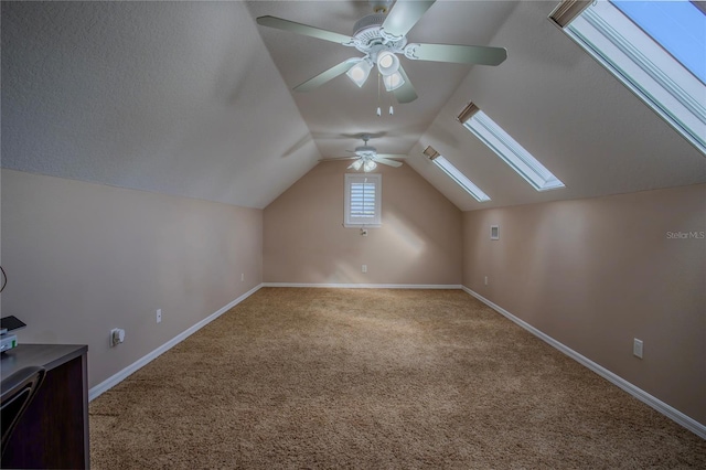 bonus room with baseboards, carpet flooring, vaulted ceiling with skylight, a textured ceiling, and a ceiling fan